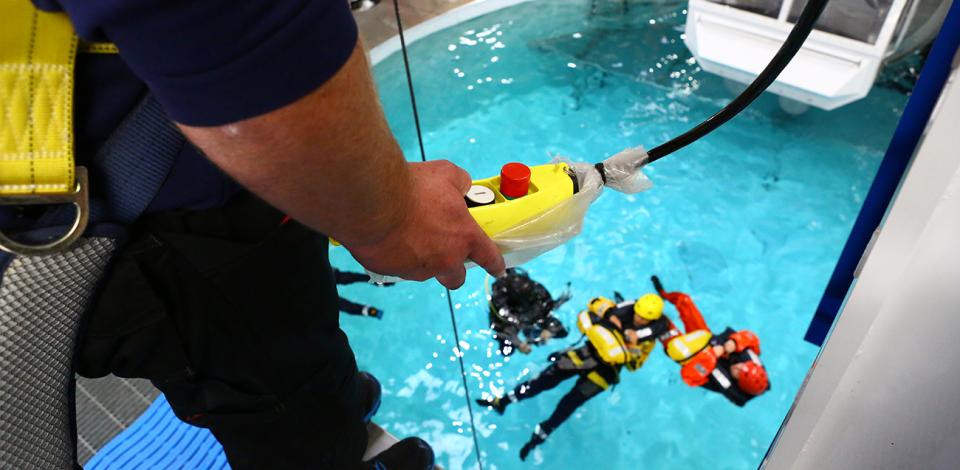 the trainer activates the remote control to heliwinch the trainees out of the water. The trainees wait their turn in the water in a safe position.